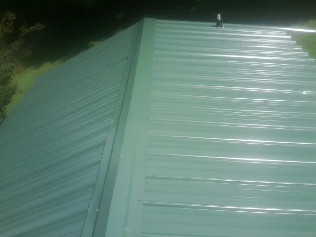 New green metal panels meeting at the ridge of a roof — Flat Roof Repair work by our crew in Brimfield