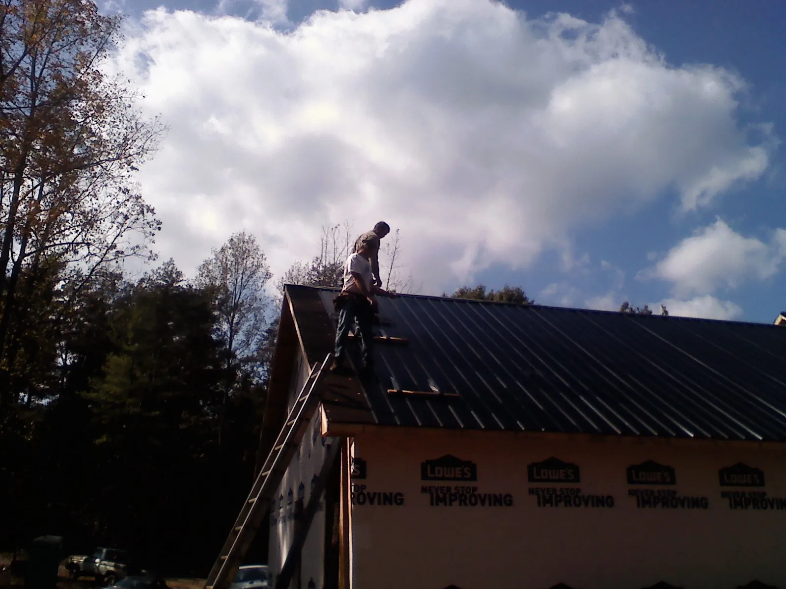 Roofer fastening dark metal panels high against a cloudy sky, from a Roof Inspection job in Brimfield