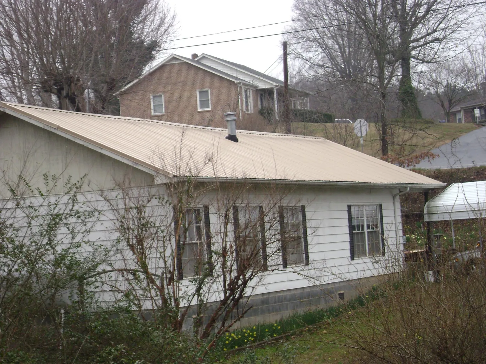 Tan metal roof on a white sided house set into a hillside — Commercial Roofing by Roofing Brothers in Brimfield