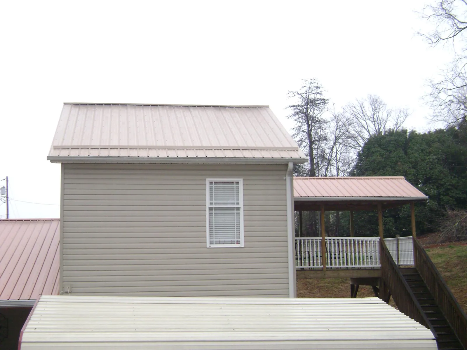 Tan metal roofs on a two story addition and attached porch, from a Roof Replacement job in Brimfield